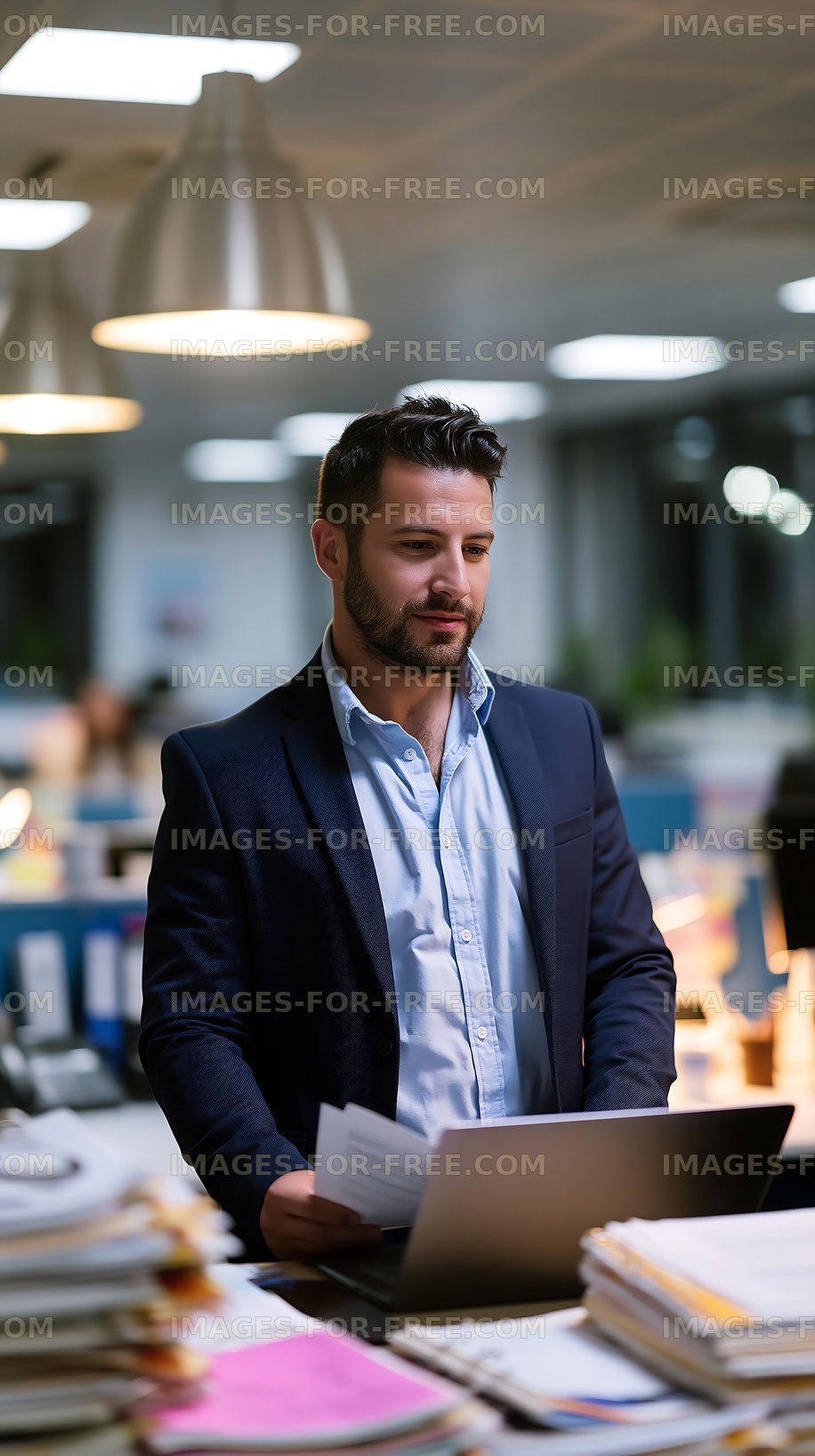 Man stands at desk with laptop in busy office setting