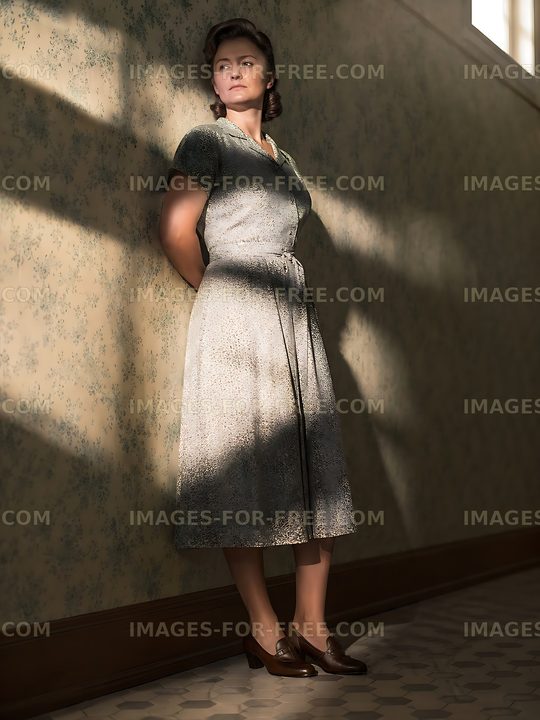 Woman in a vintage dress standing in a sunlit hallway