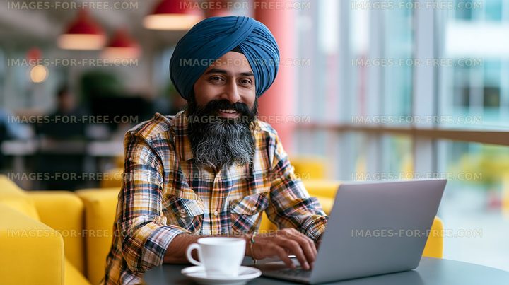 Man with turban working on laptop in modern cafe